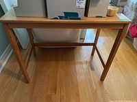 Front view of the IKEA wooden desk table showing the tabletop and leg structure on a hardwood floor.