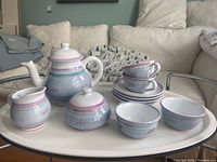 Full view of ceramic tea service set placed on oval white tray showing teapot, sugar bowl, creamer, stacked cups, saucers, and plates.