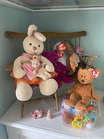 Three Beanie Babies bears on wooden doll bench with two small plastic figures in front on white surface.