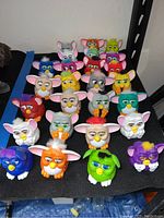 Photo showing 26 McDonalds Furby toys arranged in rows, showcasing various colors and expressions, approximately 3 inches tall each.