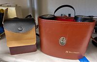 Bell & Howell binoculars in their brown leather case, showing the exterior with clasp and brand name.