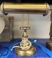 Photo showing the front view of the vintage brass desk lamp with coiled white power cord around its base and cylindrical shade horizontally positioned.