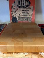 Front view of the wooden cutting block sitting in front of original box showing block surface and packaging paper underneath.