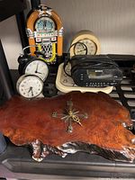 Photo showing the mixed collection of vintage and MCM clocks including two vintage twin bell alarm clocks, a burl wood wall clock, Sony digital alarm clock, decorative jukebox style clock, and another cream tabletop clock. Clocks are arranged on black shelving.