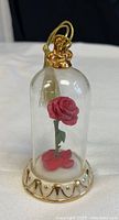 Ornament with pink rose inside glass dome, gold base and tassel from the front