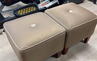 Pair of beige Ethan Allen ottomans showing top and side views with visible fabric stains and wooden legs.