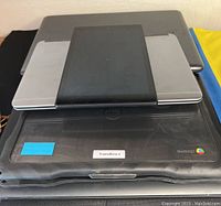 Stack of laptops and a tablet showing Dell Latitude laptops, Chromebook, and a tablet on top