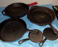 Top view showing six cast iron skillets of various sizes including two very small ones and one with red silicone handle cover.