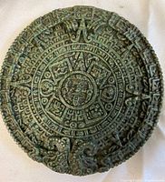 Front view of round Mayan calendar plaque showing detailed central face and surrounding glyphs in green patina finish.