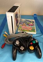 White Nintendo Wii console, black controller, Kirby's Dream Land game case, and AV cable arranged on blue background.