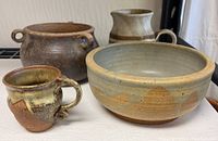 Group photo showing five pottery items including bowl, mug, pot, and pitchers on a white surface.