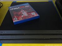 Sony PS4 console with NBA 2K16 game case on top, showing front side with Sony and PS4 branding.