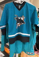 Photo of adult San Jose Sharks teal hockey jersey with shark logo and CCM branding, showing wear and holes.