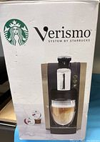 Front of the Starbucks Verismo coffee machine box showing the machine, coffee cup with layered espresso and latte, and Starbucks logo.