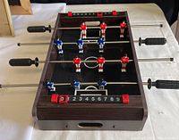 Top angle view of compact tabletop foosball table showing red and blue figures on metal rods, black handles, and score counters.