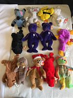 Overview photo showing 13 different Beanie Babies including bears, birds, donkey and other animals, all with hang tags and in cases.