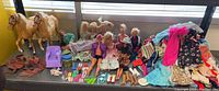 Wide shot showing two Palomino horses, multiple Barbie dolls, and a variety of Barbie clothes and shoes spread out on a shelf