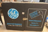 Front view of large vintage black metal tool box with GE logo and 'Performance Television' text, plus latch closure.