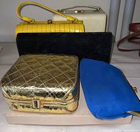 Group view of six vintage clutch handbags showing different styles, colors, and materials.