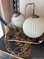 Pair of vintage white ribbed glass globe lamps with brass-tone metal caps and long brass chains, resting on a shelf.