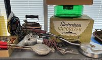 Photo showing multiple vintage household appliances including clothes irons, bed warmer, hair dryer, and the Electresteem Vaporizer in original box