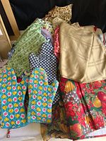 Full view of assorted vintage kitchen linens including colorful oven mitts, tablecloths, aprons, and towels stacked together showing a variety of patterns and colors.