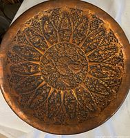 Full view of the circular tray showing the intricate embossed peacock design at the center surrounded by radiating floral patterns on a copper-toned metal surface with patina.