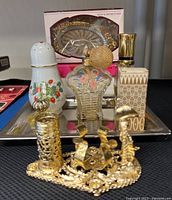 Front view showing vintage perfume bottles of various shapes and a porcelain jar with floral design and gold trim on a rectangular metal tray, plus unopened soap and tissue dish packaging.