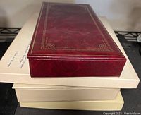 Four stationery kits stacked, with top one a red decorative box with gold trim.