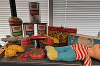 Collection view showing Remco science kit tins, red tin rotary phone, Midway bingo wheel box, yellow duck toy, and two vintage dolls with clothes.