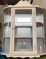 Front view of vintage wall-mounted curio cabinet with curved top and glass door revealing mirrored back and wooden shelves.