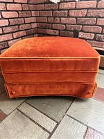 Side view of burnt orange velvet footstool showing soft fabric upholstery and one side skirt with minor repair area.