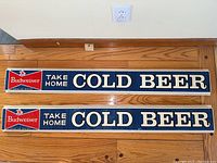 Photo showing both Budweiser signs side by side on the floor, displaying the full length and design of each sign.