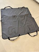 Full view of gray dog car seat cover laid flat on ground showing overall size, shape, black adjustable straps, seat belt slits and pocket flaps
