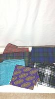 Various fabric cuts including wool tartan plaids and printed cottons laid out flat on a white background.