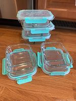 Set of 5 glass food storage containers stacked and arranged on wood surface, showing turquoise locking lids.
