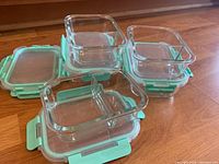 Five rectangular clear glass food storage containers with light blue plastic locking lids with four side clips, one container showing the divider inside.