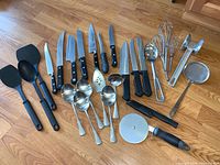 Full set of knives, kitchen utensils, flatware and tools arranged on wooden floor