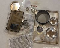 Overview of large lot containing baking sheets, cooling racks, mixing bowls, small chopper, funnels and more baked related items.