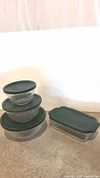 Photo showing 3 nested Pyrex glass bowls stacked with dark green lids and a glass loaf pan with a dark green lid alongside them.