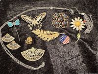 Full display of vintage jewelry pieces on black fabric background showing all pins, brooches, earrings, and necklace in lot