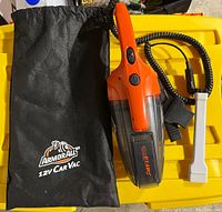Full view of the Armor All 12V car vacuum cleaner with power cord and storage bag on yellow surface