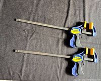 Two Irwin Quick-Grip clamps laid flat on a dark cloth background showing blue and yellow triggers and metal bars.