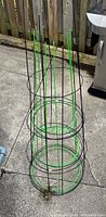 Three metal tomato plant cages stacked together outdoors on concrete by wood fence and grill.