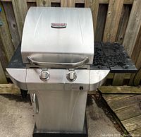 Front view of stainless steel BBQ with two burners and closed lid showing side shelves and control knobs.