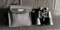 Photo showing Bushnell branded black binocular case next to binoculars