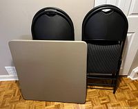 Card table and four folding chairs arranged standing against wall showing table top and chair backrests
