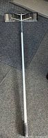 Photo of expandable snow rake laid flat with telescoping pole and wide metal rake head.