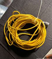 Photo showing a coiled yellow extension cord with visible metal connector at one end against a dark background.