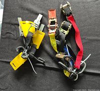 Photo showing multiple tie down straps in various colors and hardware types placed on a dark surface.
